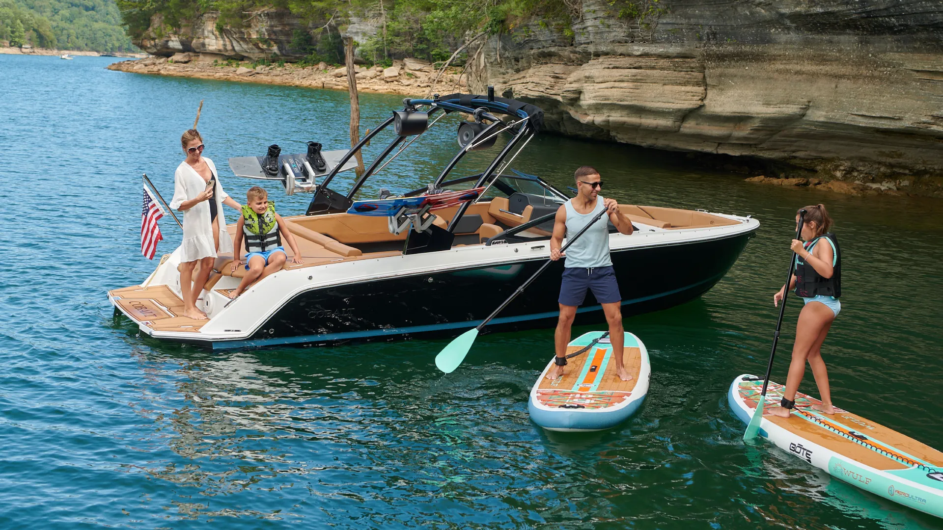people on the back of the boat and people paddle boarding nearby