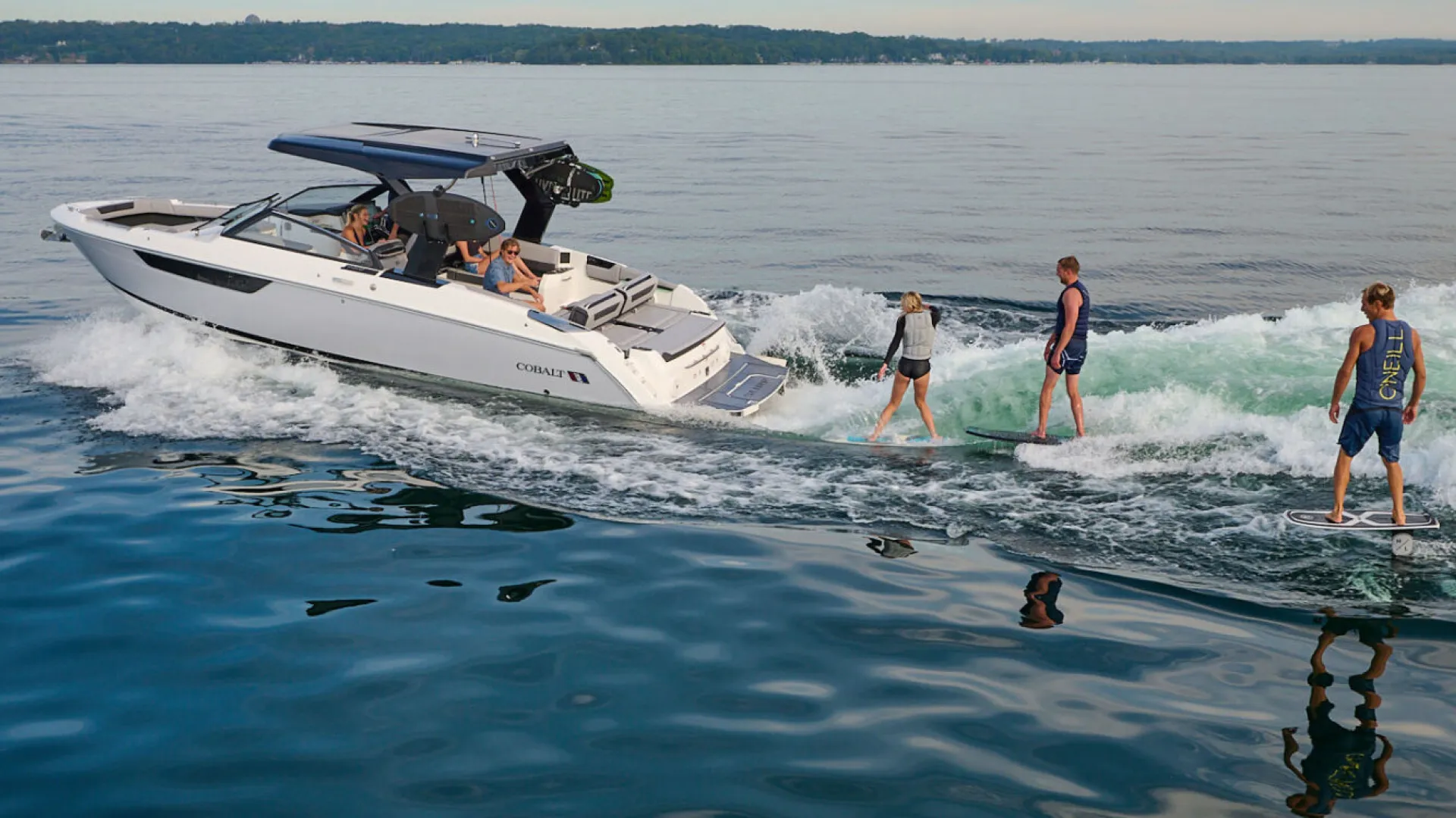 boat in water with 3 people wakesurfing behind it 